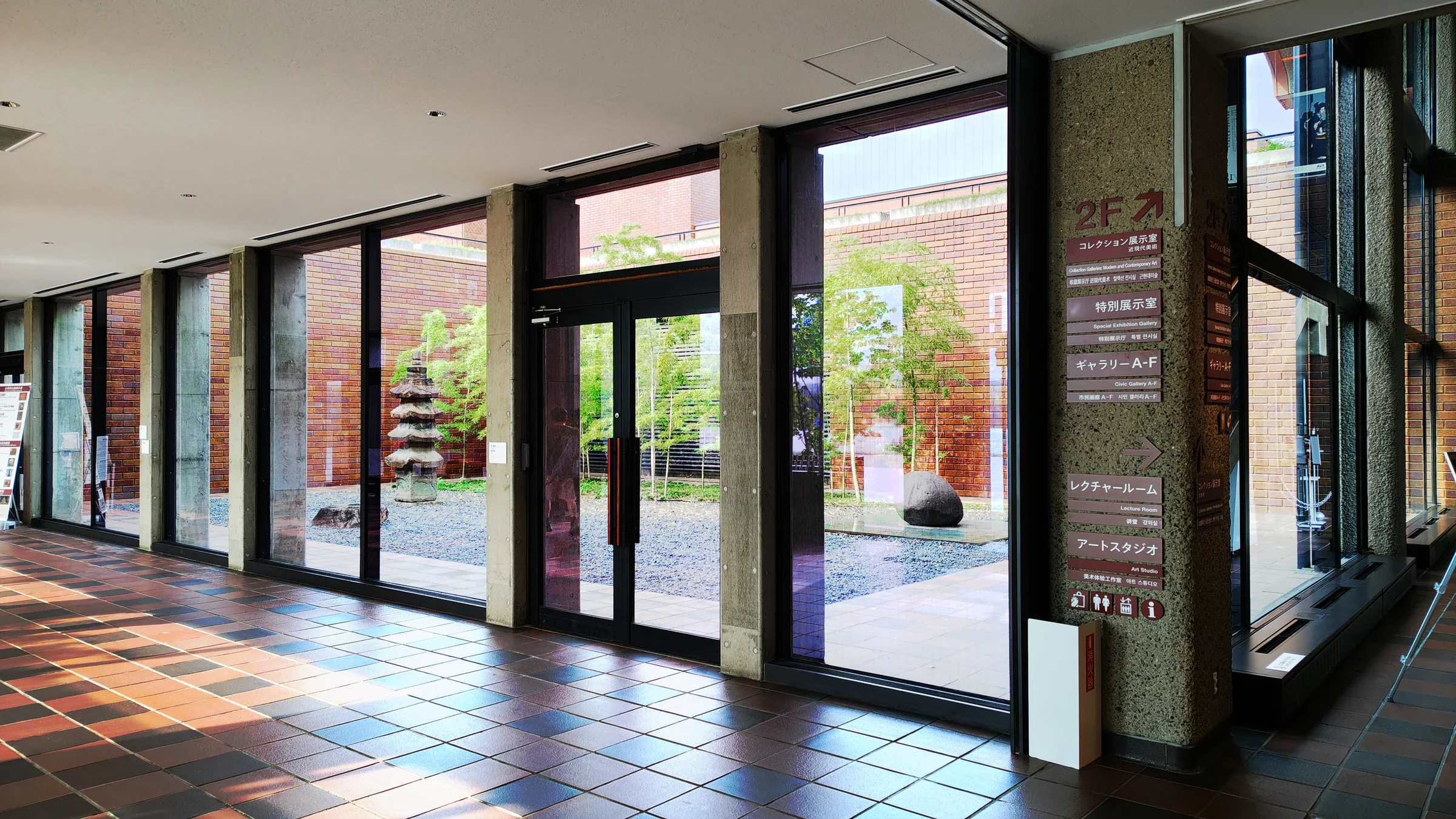 福岡市美術館中庭的展室方向指示，標示二樓收藏展室與一樓藝術工作室