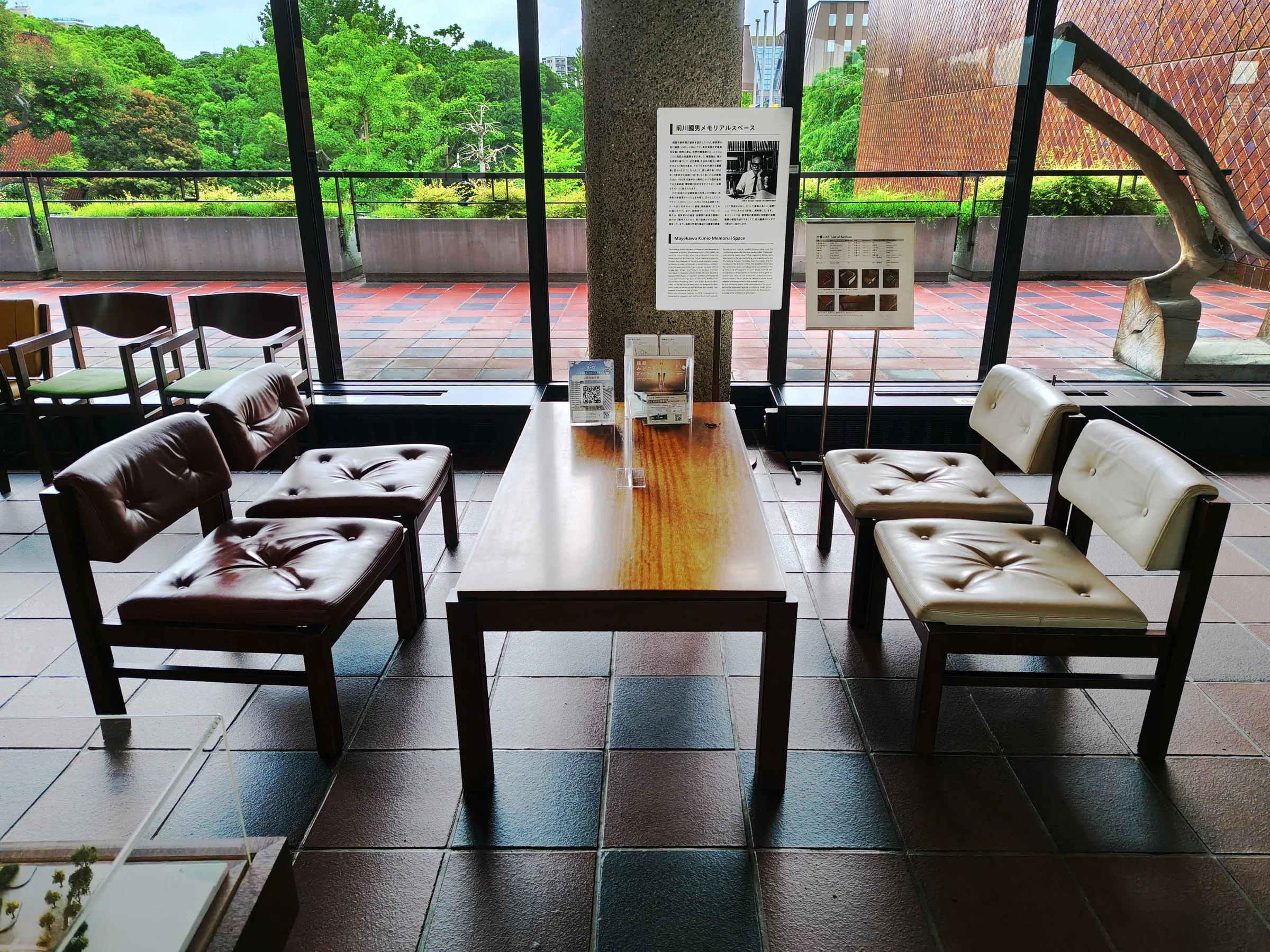 福岡市美術館大廳的座椅與長桌，落地窗外是綠樹和館舍外牆