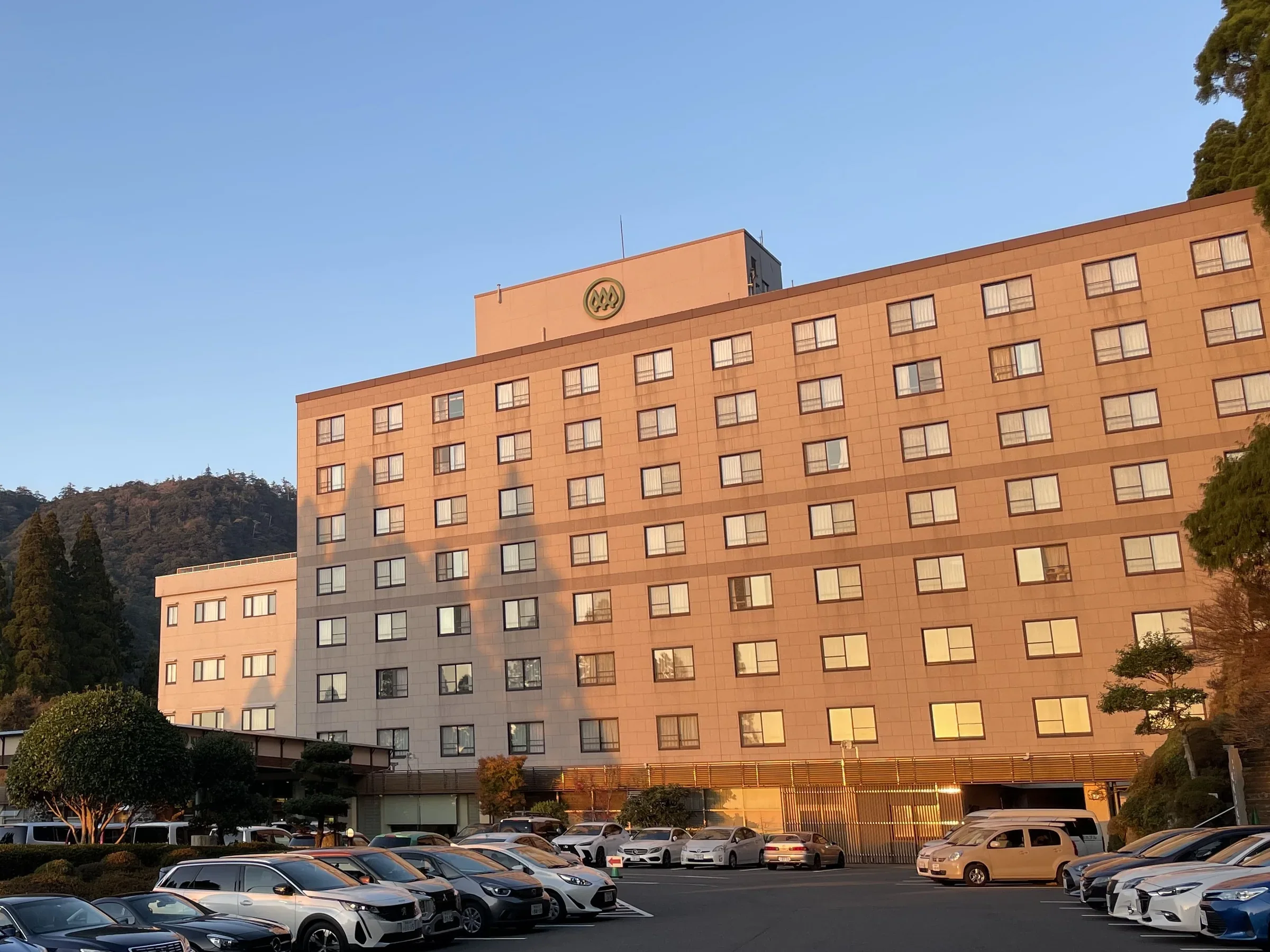 霧島酒店多層客房外牆與前方停車場，背景是霧島山林