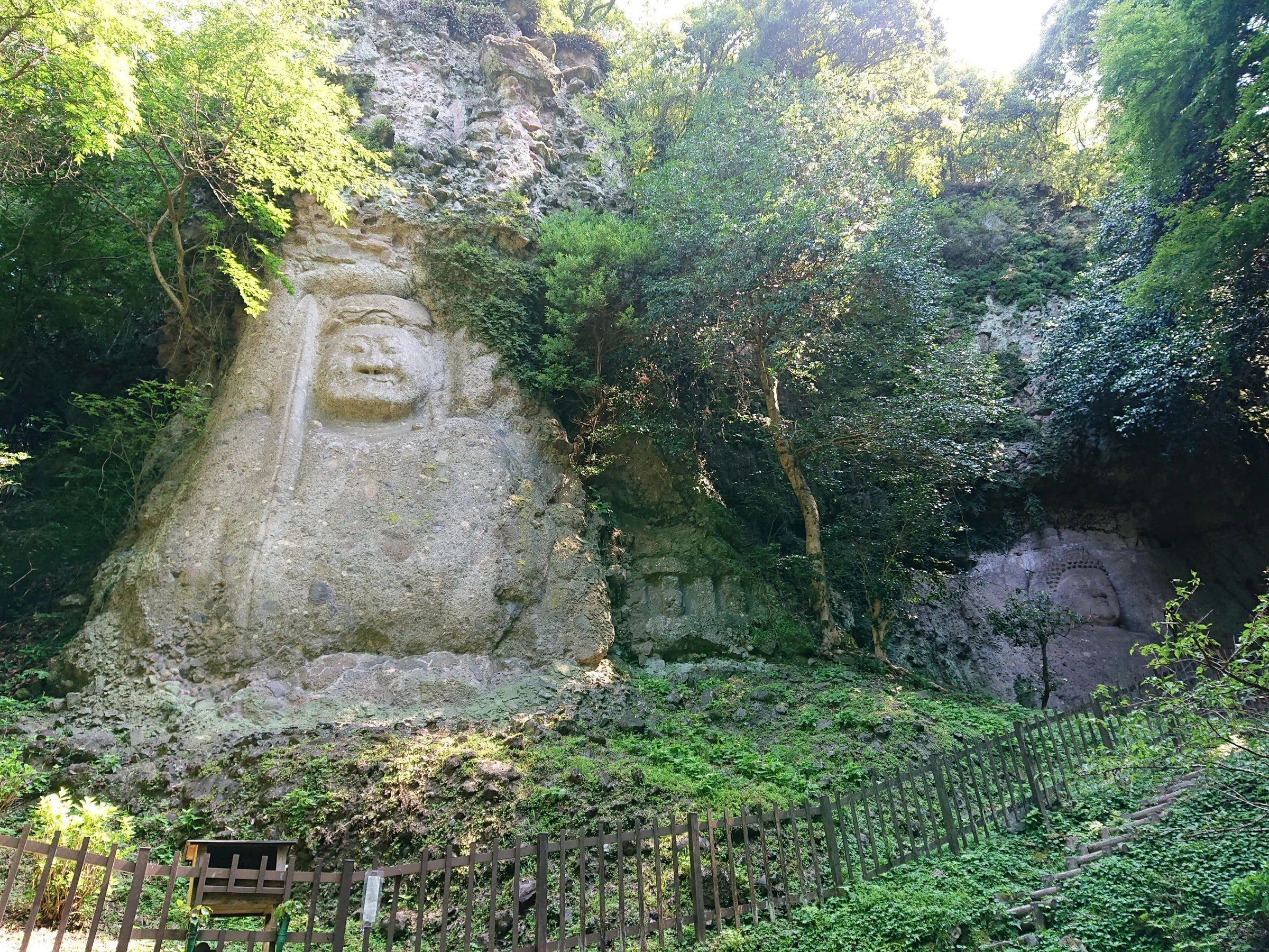 熊野磨崖佛兩尊岩壁佛像同框，前景有樹木及護欄