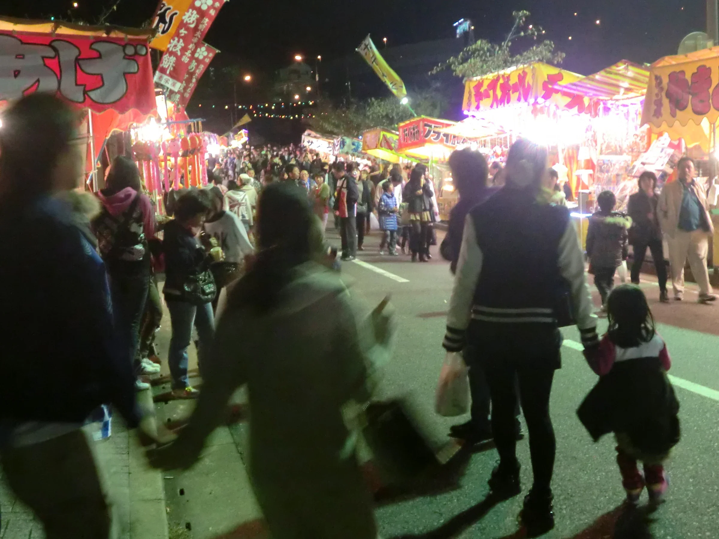 起業祭夜間縁日的攤位亮起燈光，遊戲攤與來往人潮沿路排列