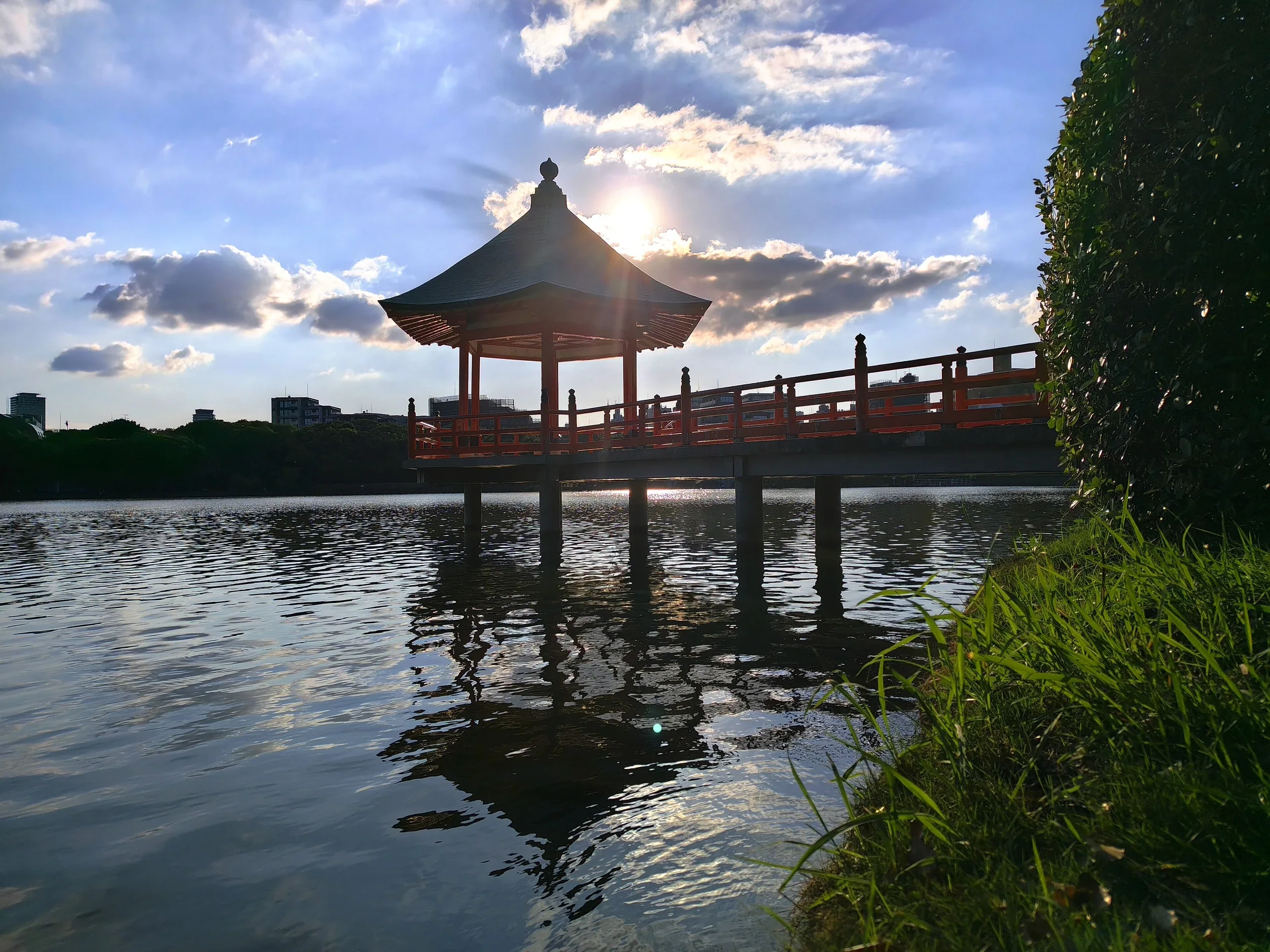 夕陽映在大濠公園浮見堂與湖面，紅色橋欄沿著水面延伸