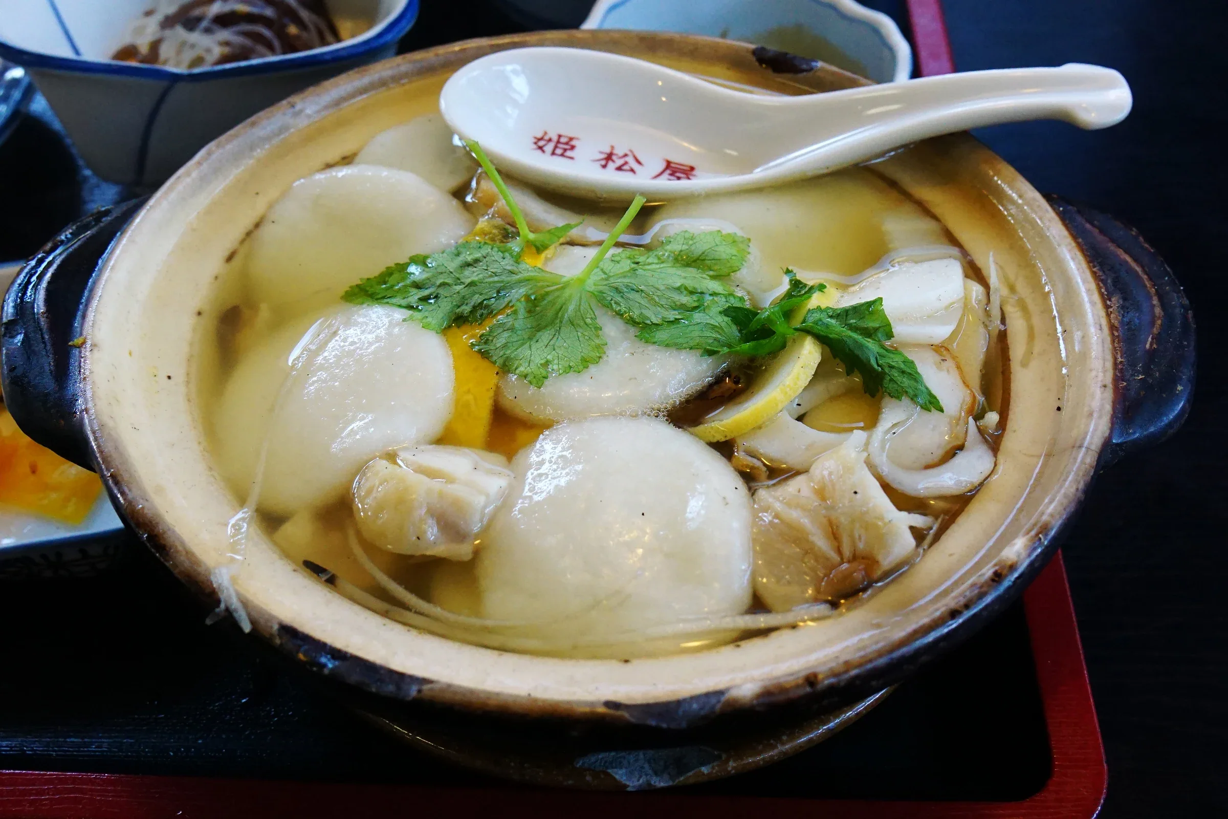 姫松屋本店的島原具雜煮，土鍋內有丸餅、青菜，旁邊放著店名湯匙